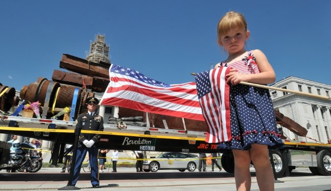 girl holding US flag poses in front of steel wreckage from the 9/11 tragedy